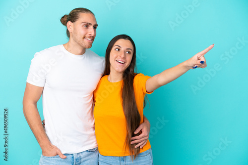 Young caucasian couple isolated on blue background pointing finger to the side and presenting a product