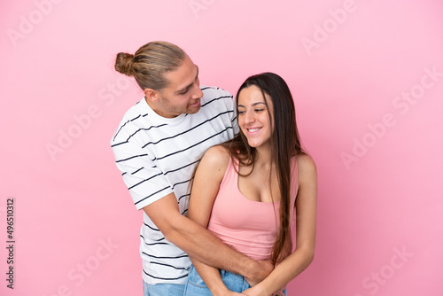 Young caucasian couple isolated on pink background hugging