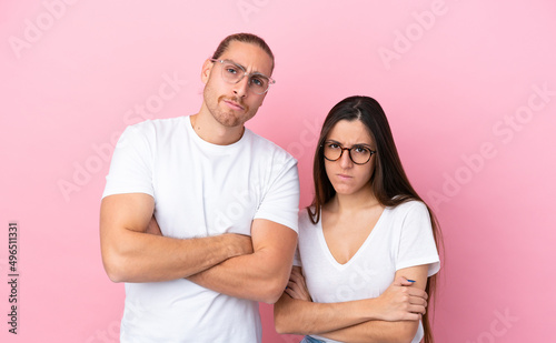Young caucasian couple isolated on pink background With glasses and arms crossed