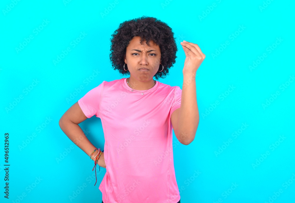young girl with afro hairstyle wearing pink T-shirt over blue background angry gesturing typical italian gesture with hand, looking to camera young girl with afro hairstyle wearing pink T-shirt over blue background angry gesturing typical italian gesture with hand, looking to camera
