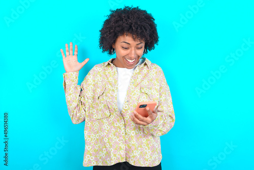 young girl with afro hairstyle wearing floral shirt over blue background holding in hands cell reading browsing news photo