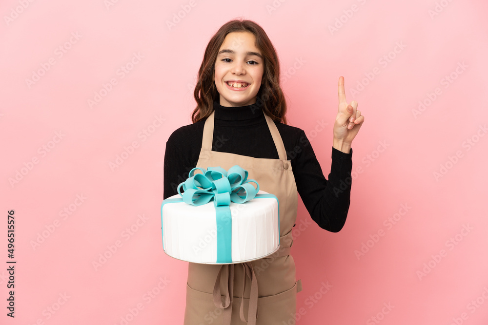 Little Pastry chef holding a big cake isolated on pink background pointing up a great idea Little Pastry chef holding a big cake isolated on pink background pointing up a great idea