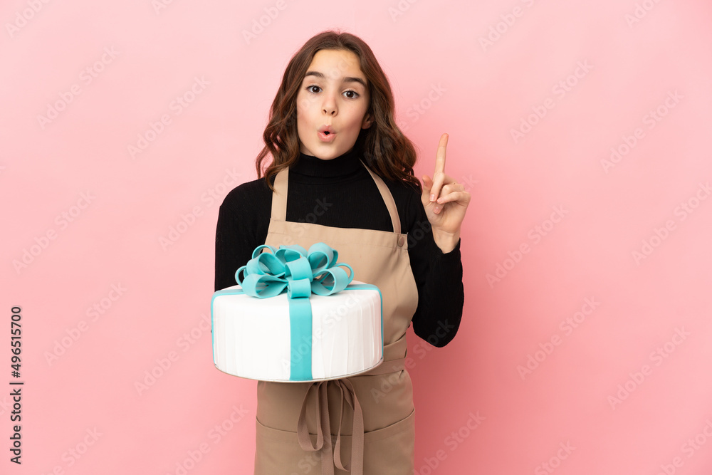 Little Pastry chef holding a big cake isolated on pink background intending to realizes the solution while lifting a finger up Little Pastry chef holding a big cake isolated on pink background intending to realizes the solution while lifting a finger up