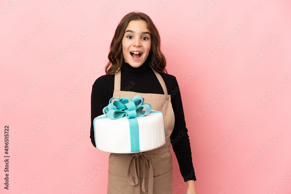 Little Pastry chef holding a big cake isolated on pink background with surprise facial expression Little Pastry chef holding a big cake isolated on pink background with surprise facial expression