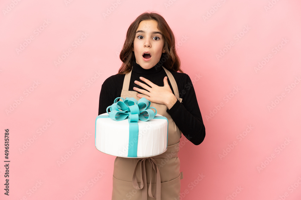 Little Pastry chef holding a big cake isolated on pink background surprised and shocked while looking right Little Pastry chef holding a big cake isolated on pink background surprised and shocked while looking right