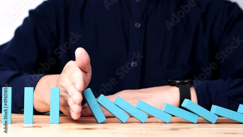 Businessman hand stopping continuous failing domino wooden effect. Concept of Risk Management, Business Crisis, Domino Effect, Investment, Finance, Risk, Disaster, Protection, Prevention, Opportunity