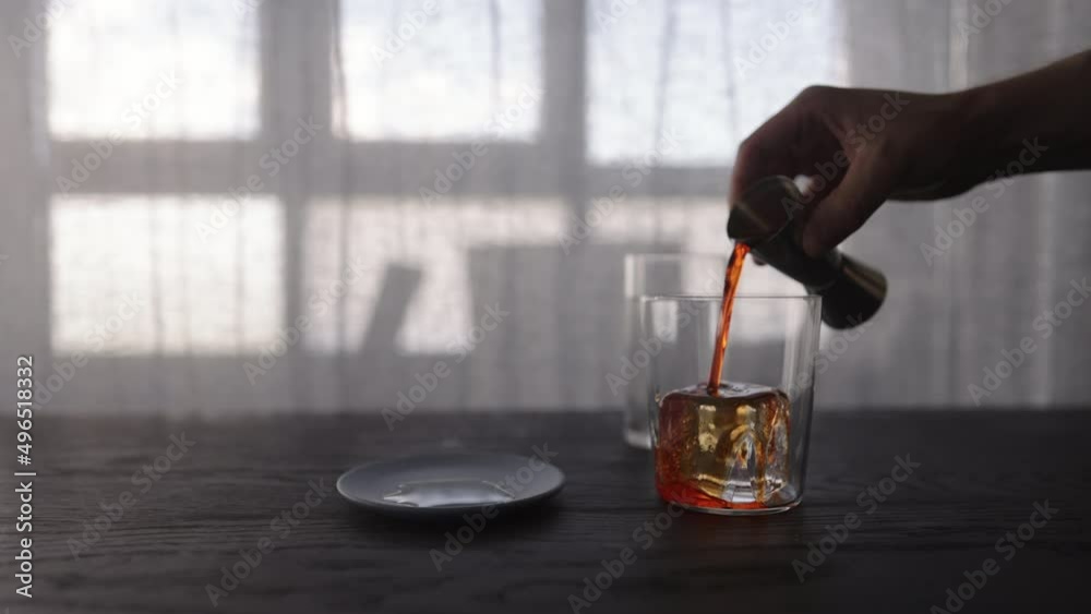 Slow motion pour orange syrup over ice ball in tumbler glass on wood table Slow motion pour orange syrup over ice ball in tumbler glass on wood table