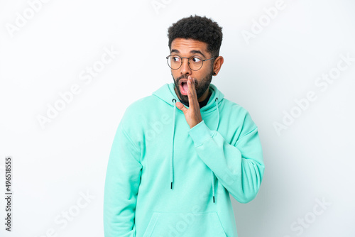 Young Brazilian man isolated on white background whispering something with surprise gesture while looking to the side