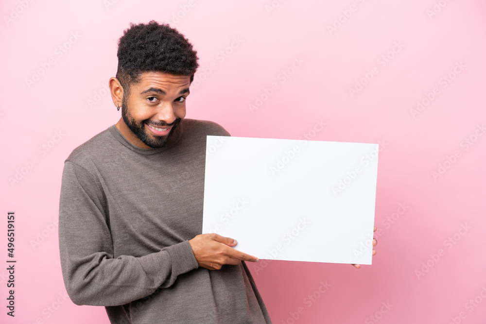 Young Brazilian man isolated on pink background holding an empty placard with happy expression