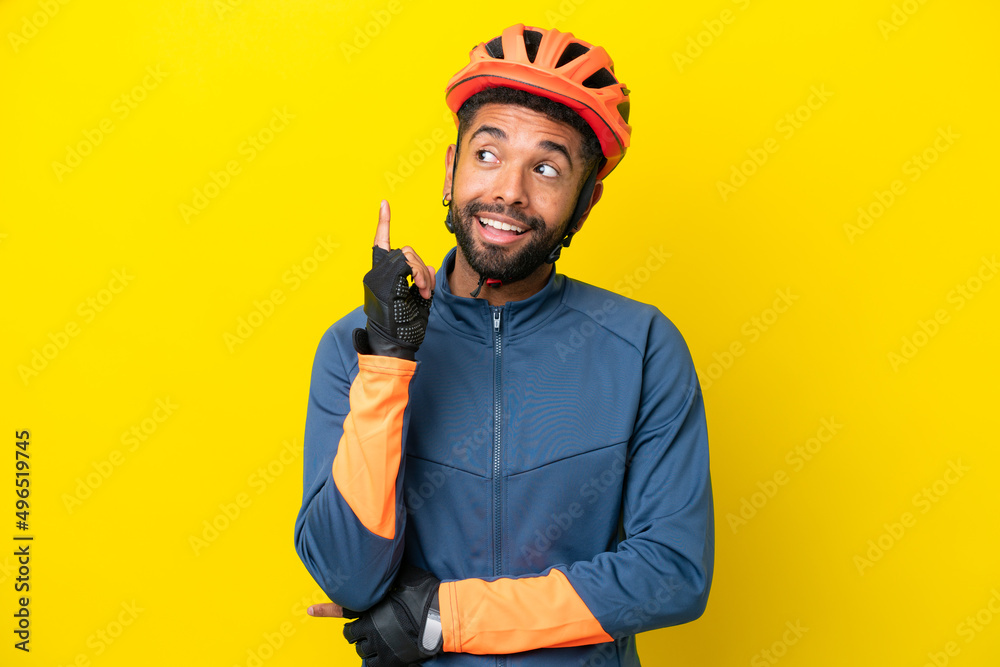 Young cyclist Brazilian man isolated on yellow background thinking an idea pointing the finger up