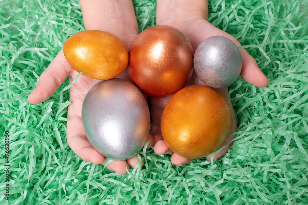 Fototapeta premium Children's hands holding multi-colored eggs on a paper green like grass background. Easter concept