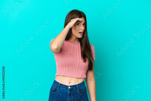 Young Brazilian woman isolated on blue background doing surprise gesture while looking to the side