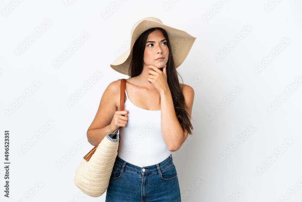 Young Brazilian woman with Pamela holding a beach bag isolated on white background having doubts and with confuse face expression Young Brazilian woman with Pamela holding a beach bag isolated on white background having doubts and with confuse face expression