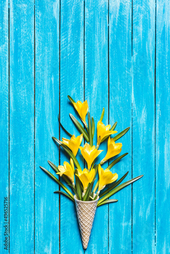 Yellow flowers in ice cream cone on a turquoise wooden background