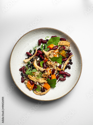 Chicken salad with quinoa, black beans, kidney beans,  pumpkin, fresh herbs. On a ceramic plate, with a white  background photo