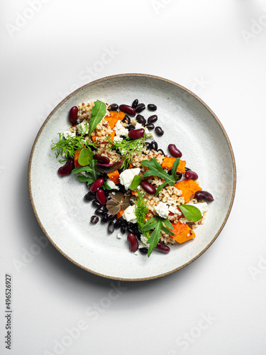 Quiona salad with  cheese, black beans, red beans,  pumpkin, herbs. On a ceramic plate, with a white background photo