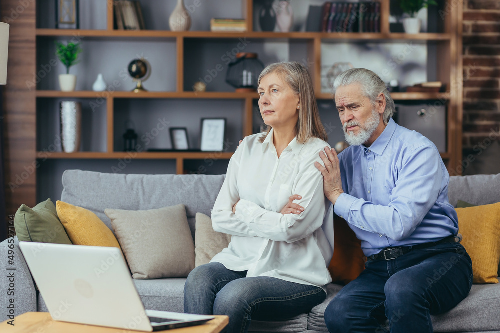 A quarreling couple, a gray-haired man and a woman are sitting on the couch talking to a family psychologist, using a laptop for a video call A quarreling couple, a gray-haired man and a woman are sitting on the couch talking to a family psychologist, using a laptop for a video call