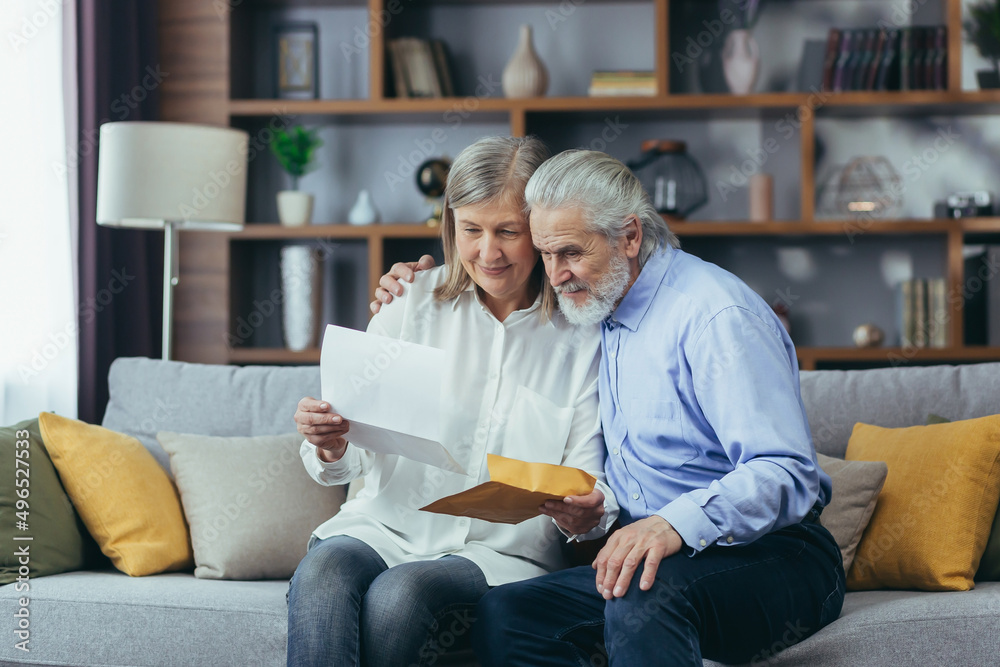 Happy senior retired couple sitting on sofa at home reading letter, happy and smiling Happy senior retired couple sitting on sofa at home reading letter, happy and smiling