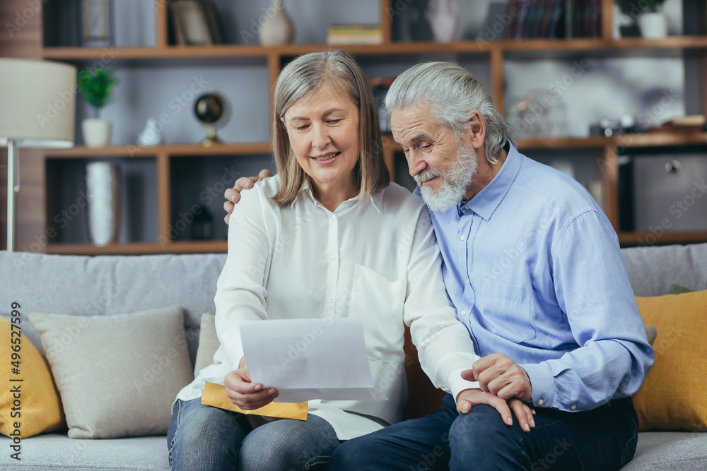 Happy senior retired couple sitting on sofa at home reading letter, happy and smiling Happy senior retired couple sitting on sofa at home reading letter, happy and smiling