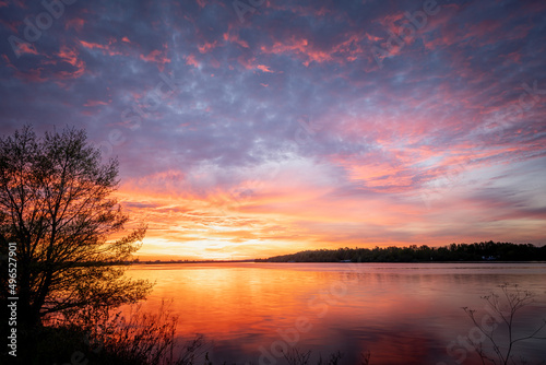 Beautiful sunset, sky with clouds above lake with trees around.