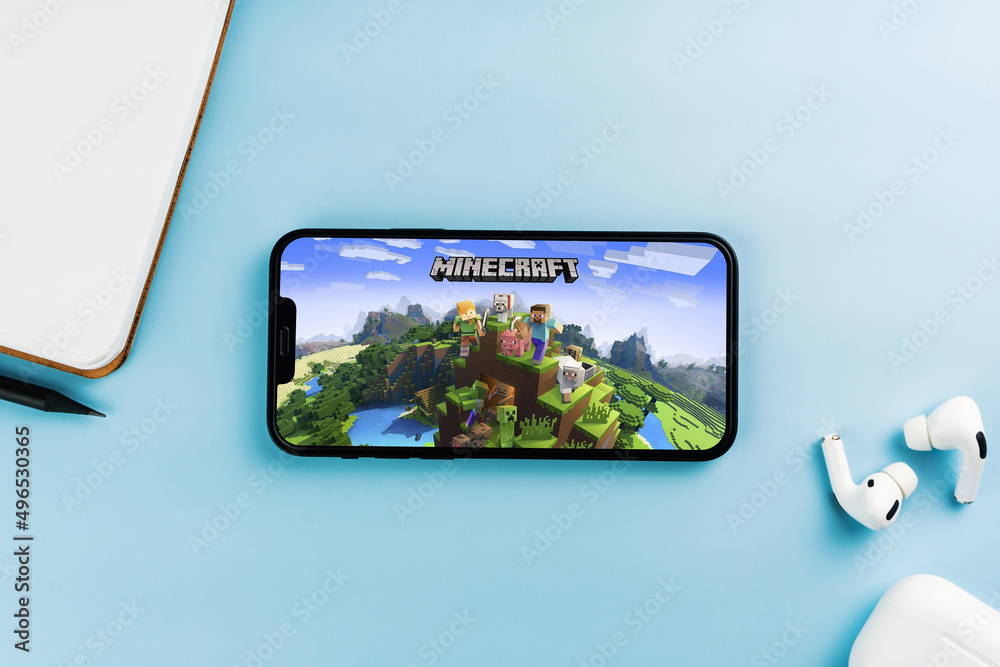 Fototapeta premium Minecraft mobile game app on the smartphone screen. Blue background with notepad and AirPods. Rio de Janeiro, RJ, Brazil. April 2022.