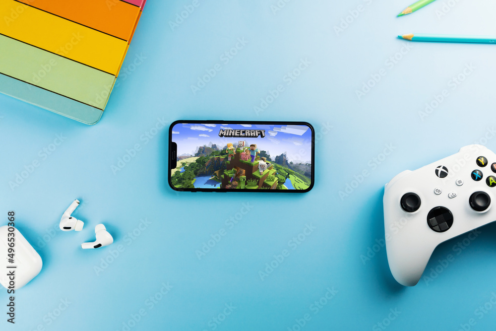Fototapeta premium Minecraft mobile game app on the smartphone screen. Blue background with school supplies, AirPods, video game controller. Rio de Janeiro, RJ, Brazil. April 2022