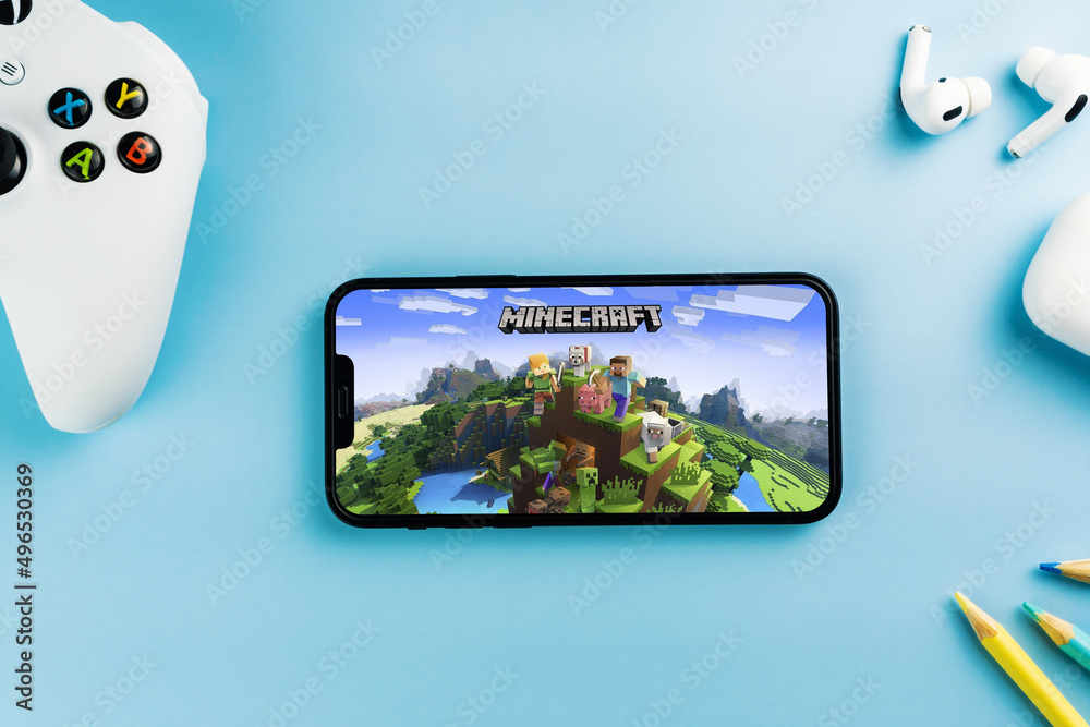 Fototapeta premium Minecraft mobile game app on the smartphone screen. Blue background with school supplies, AirPods, video game controller. Rio de Janeiro, RJ, Brazil. April 2022