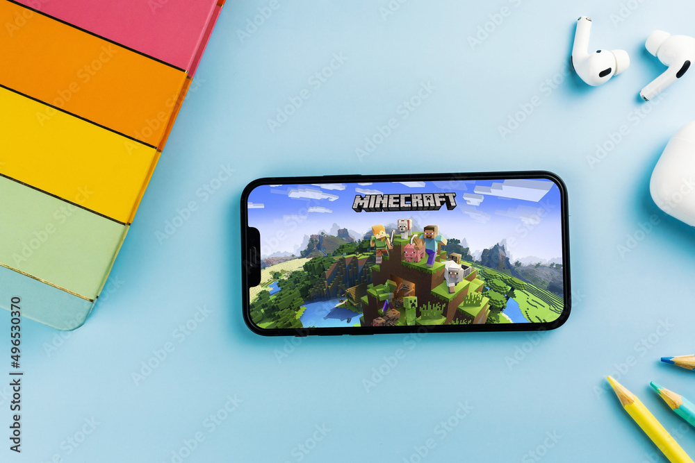 Fototapeta premium Minecraft mobile game app on the smartphone screen. Blue background with school supplies, AirPods, video game controller. Rio de Janeiro, RJ, Brazil. April 2022
