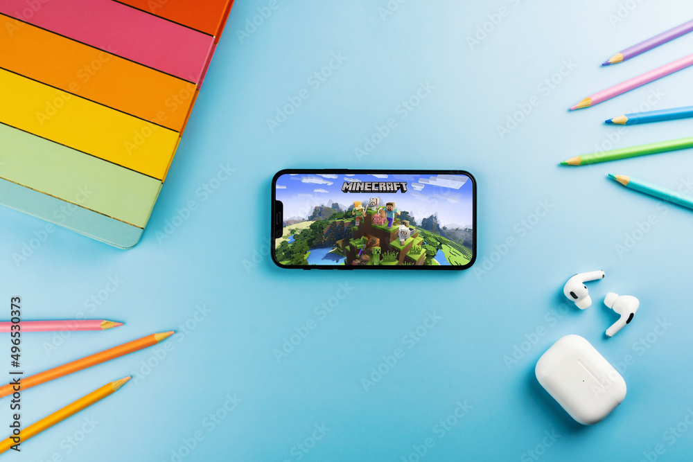 Fototapeta premium Minecraft mobile game app on the smartphone screen. Blue background with school supplies, AirPods, video game controller. Rio de Janeiro, RJ, Brazil. April 2022