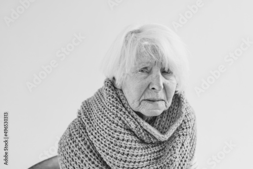 monochrome portrait of senior woman in scarf freezing cold at home. Health care, crisis, oldness concept