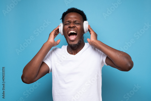 Happy emotive african man listening to music with white earphone.