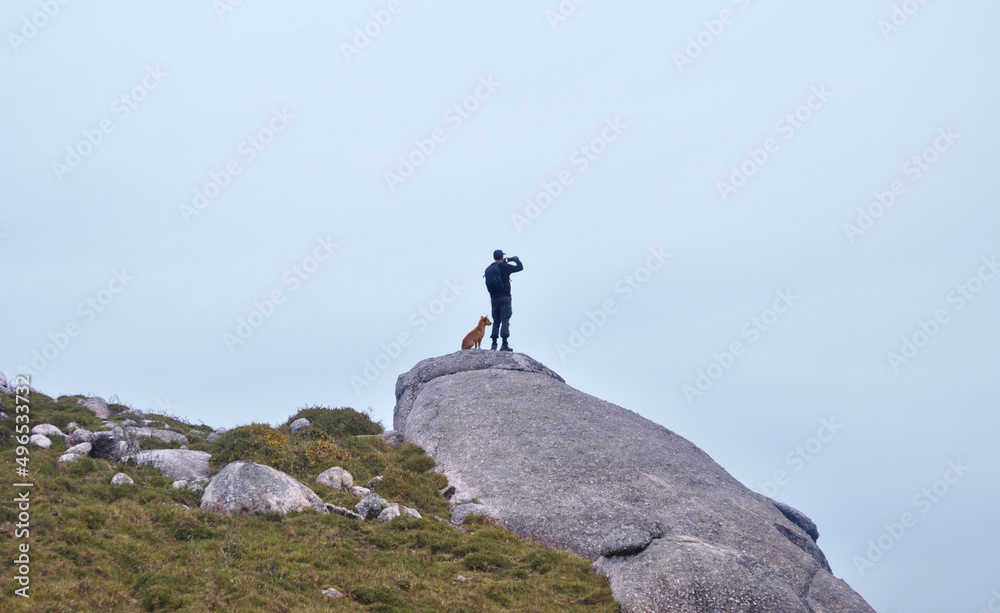 Pessoa do sexo masculino no topo de uma montanha a fotografar as vistas, cão ao lado sentado, topo de montanha, trekking, caminhar