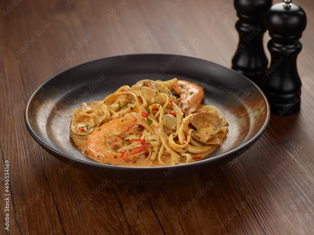 Seafood Aglio Olio Pasta in a dish isolated on dark wooden table side view singapore food Seafood Aglio Olio Pasta in a dish isolated on dark wooden table side view singapore food