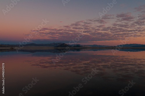Photo taken at dusk showing a mirror image of broken clouds and a mountain range on a shallow  intermittent lake  Soda Lake  in the Mojave Desert  California.