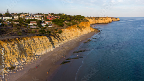 Aerial drone view of people on the beach during a beautiful sunset. Amazing vibrant colors. Algarve, Portugal. Clear waters. Holidays and Vacations. Travel and adventure. Nomad life.
