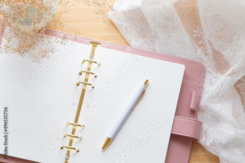Flat lay, top view of a pastel pink leather planner, dried flower bouquet and stationery on a wooden desk.