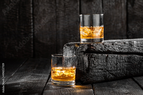 Two glasses of ice whisky on burnt boards