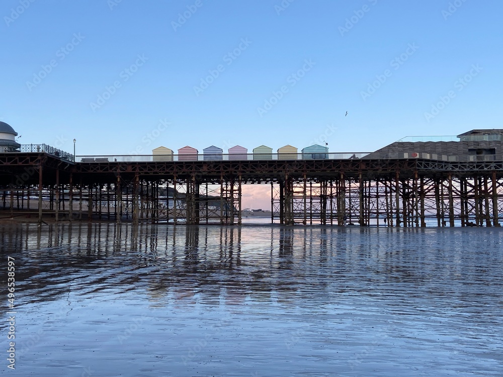 Hastings, East Sussex, UK - Hastings pier with beach huts at low tide reflections on the sand 