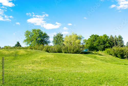 Scenic view of beautiful small mountains, hills, mounds with green grass lawn against bright blue sky with clouds in city park photo