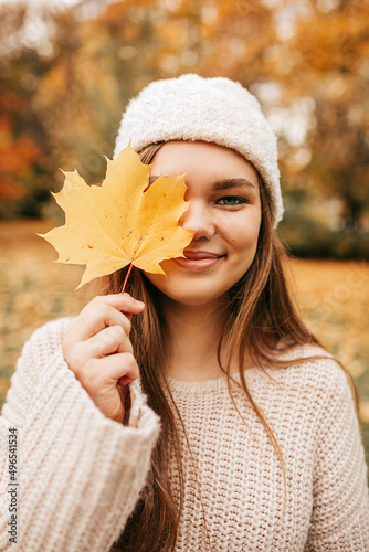Vertical portrait of close up face attractive blond smiling woman in hat  hold golden maple leaf face  close eye. Autumn