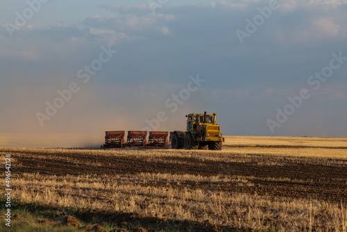 Kostanay Province, Kazakhstan - May 01, 2019: Tractor seeds wheat in field on sunset. Sowing season.