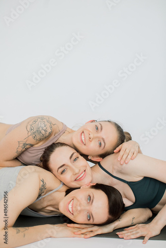 three beautiful women smiling bowed their heads over each other, hugging each other.
girls rest after yoga practice and meditate in a women's circle on a white background
