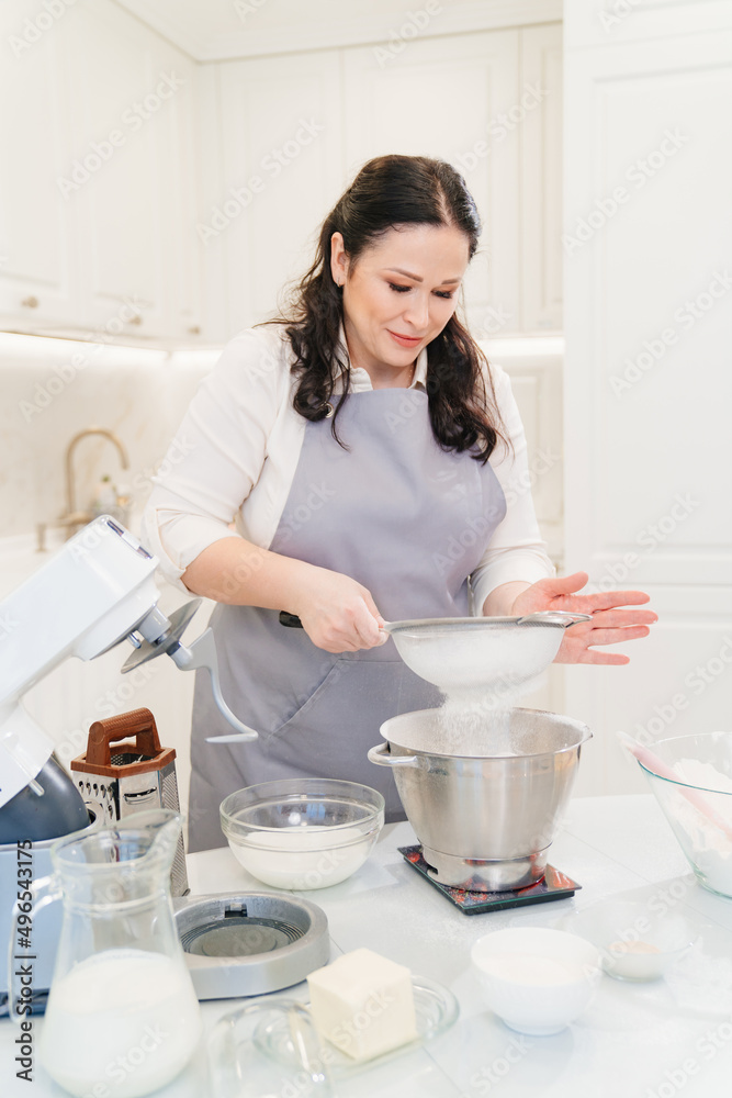 woman cook sifts flour through sieve to prepare dough in mixer bowl on scales. woman cook sifts flour through sieve to prepare dough in mixer bowl on scales.
