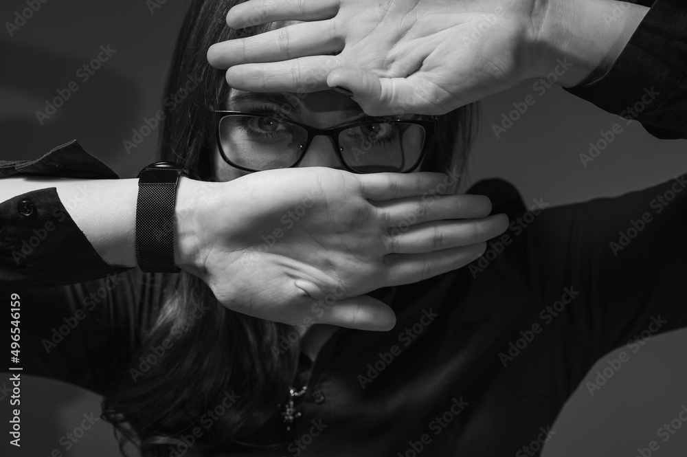 Black and white photo, close up portrait of a cheerful girl in glasses showing happiness, smiling. She covers her face with her hand so that she pierces it. Place for copy in