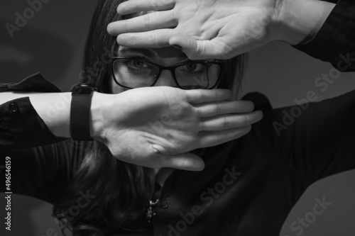 Black and white photo, close up portrait of a cheerful girl in glasses showing happiness, smiling. She covers her face with her hand so that she pierces it. Place for copy in © Jurii