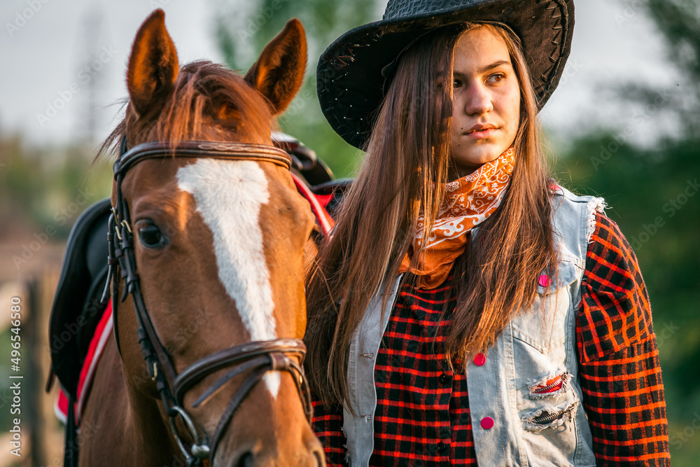 Obraz premium A cowgirl stands near her horse in a field at sunset.