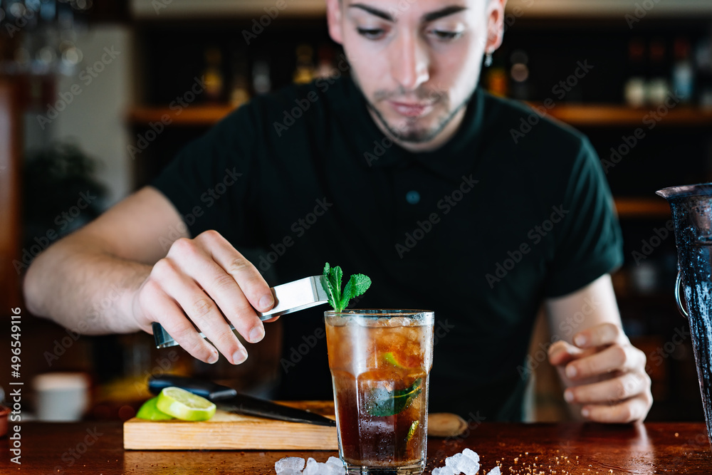 Young waiter, putting mint leaves to decorate a cocktail. Horizontal