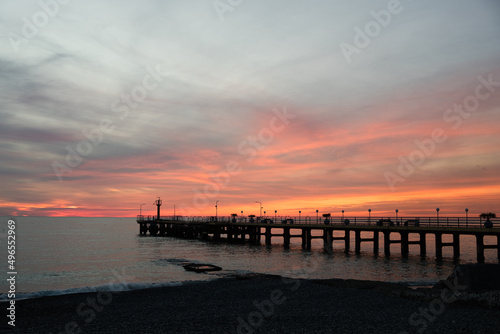Fishing pier on the ocean with a colorful and golden sunset. Ocean beach sunrise and dramatic colorful sky clouds.