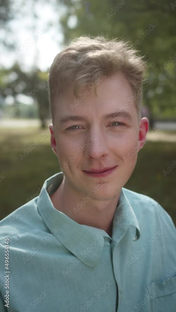A young handsome man in a blue shirt is staring at the camera, blinking his eyes and contemplating A young handsome man in a blue shirt is staring at the camera, blinking his eyes and contemplating