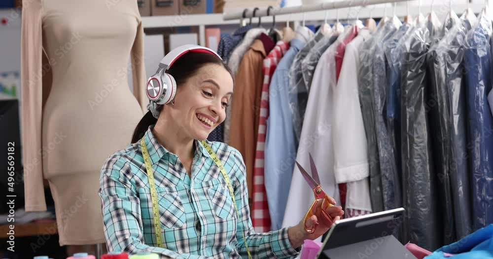 Joyful designer stylist in headphones cuts fabric in atelier Joyful designer stylist in headphones cuts fabric in atelier